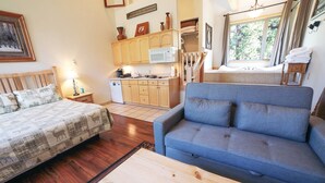 A cozy living room with a blue sofa, a wooden coffee table, and a bed with a checkered blanket. - Deluxe Spa Suite, jetted tub for 2, fireplace (Estes Park)