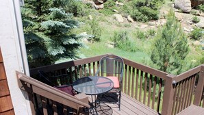 A wooden deck with a table and chairs, overlooking a rocky landscape with trees. - Deluxe Spa Suite, jetted tub for 2, fireplace (Estes Park)