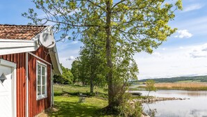 A red wooden house with a satellite dish, a grassy yard, a tree, and a calm lake.