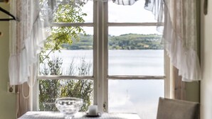 A room with a table set for two, a window with a view of a lake, and curtains.