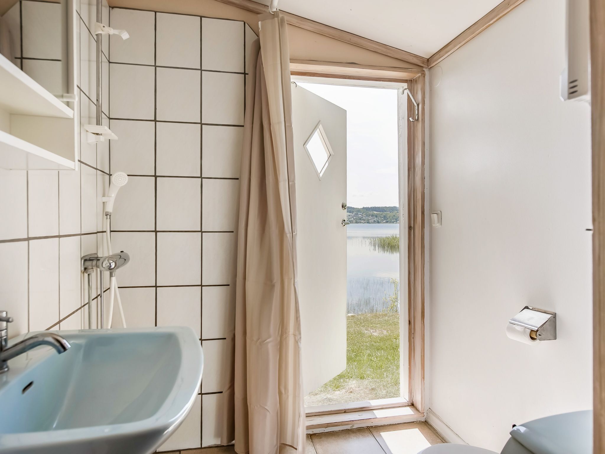 Une salle de bain équipée d’un lavabo, d’une douche et de toilettes. Elle offre une vue sur un lac et sur une maison en arrière-plan.