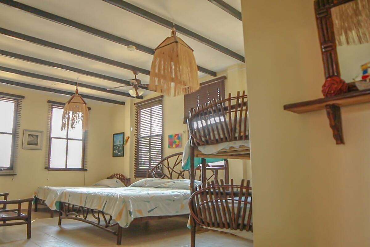 A bedroom with a bed, two chairs, a wooden bunk bed, and a ceiling fan.