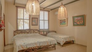 Een kamer met twee houten bedden, rieten stoelen en een hanglamp.