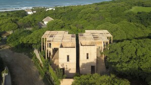 A modern building with a flat roof and rectangular structure, surrounded by dense greenery and a coastal view.