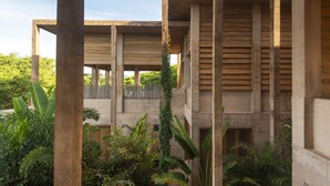 A modern building with a concrete structure, large windows, and a lush garden area.