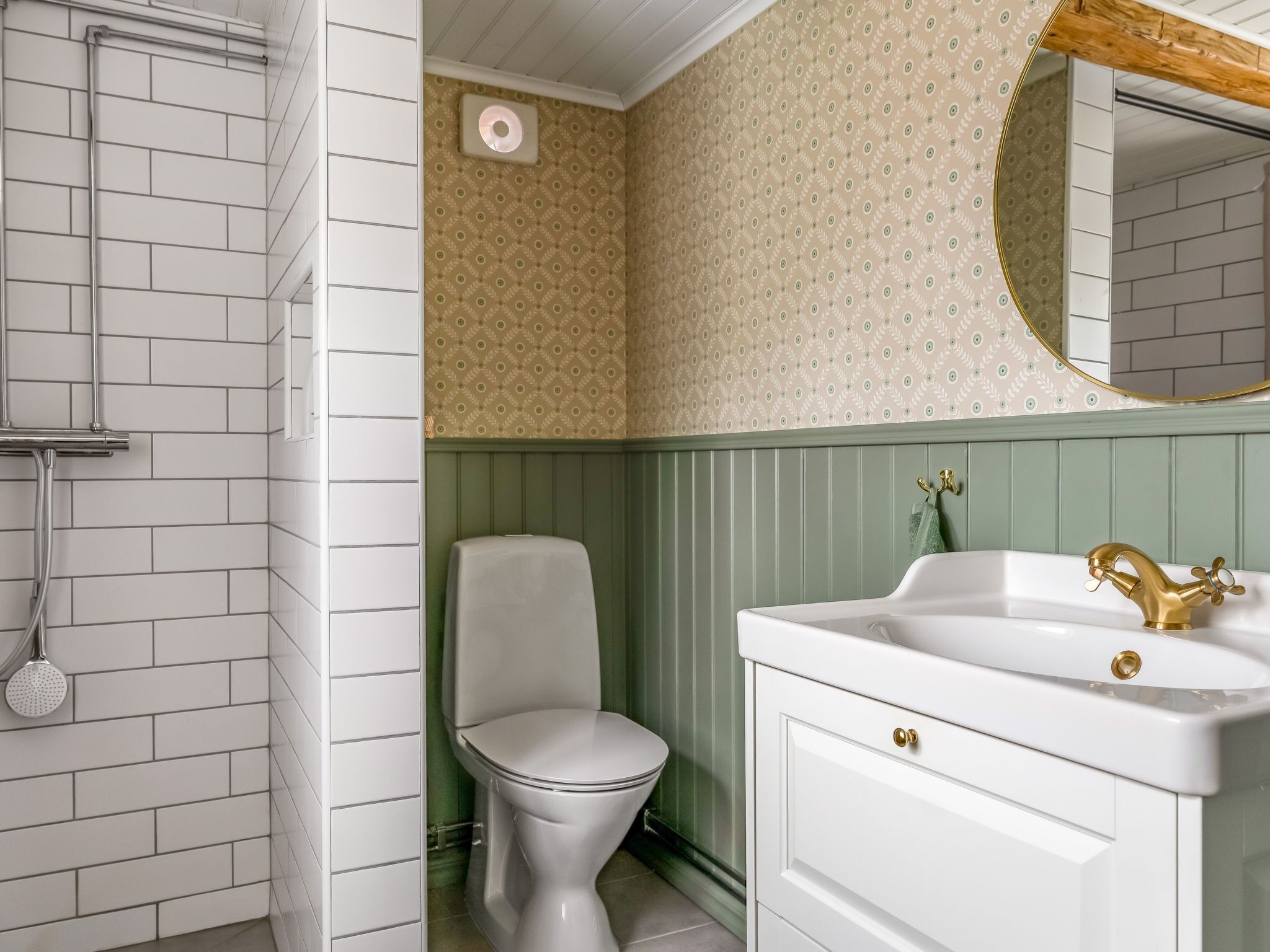 A bathroom with white tiled walls, a toilet, a sink with a gold faucet, and a mirror.