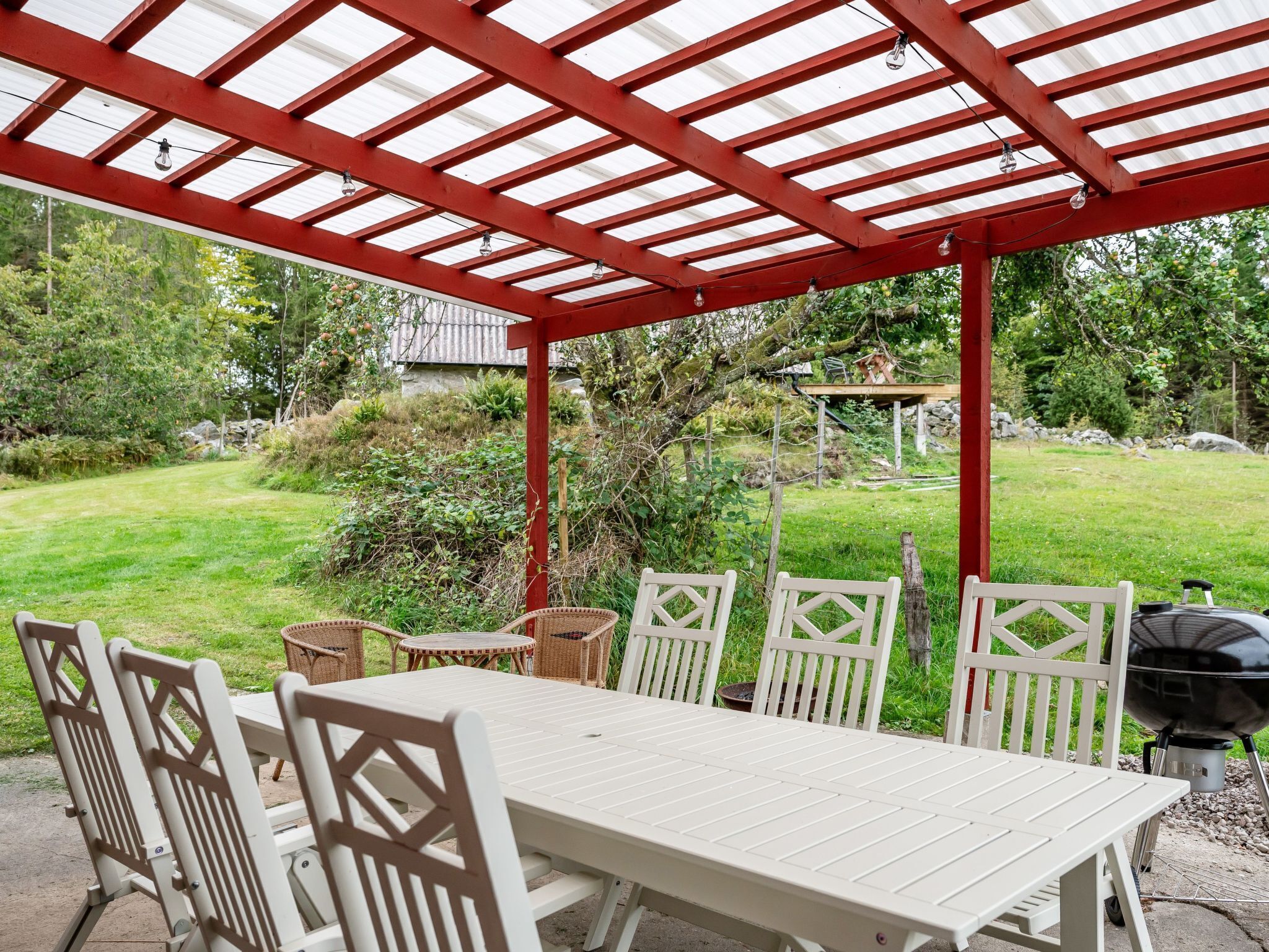An outdoor patio with a white table and chairs, a red pergola, and a barbecue grill.