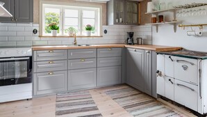 A kitchen with grey cabinets, a wooden countertop, a built-in oven, a coffee maker, and a window with plants.