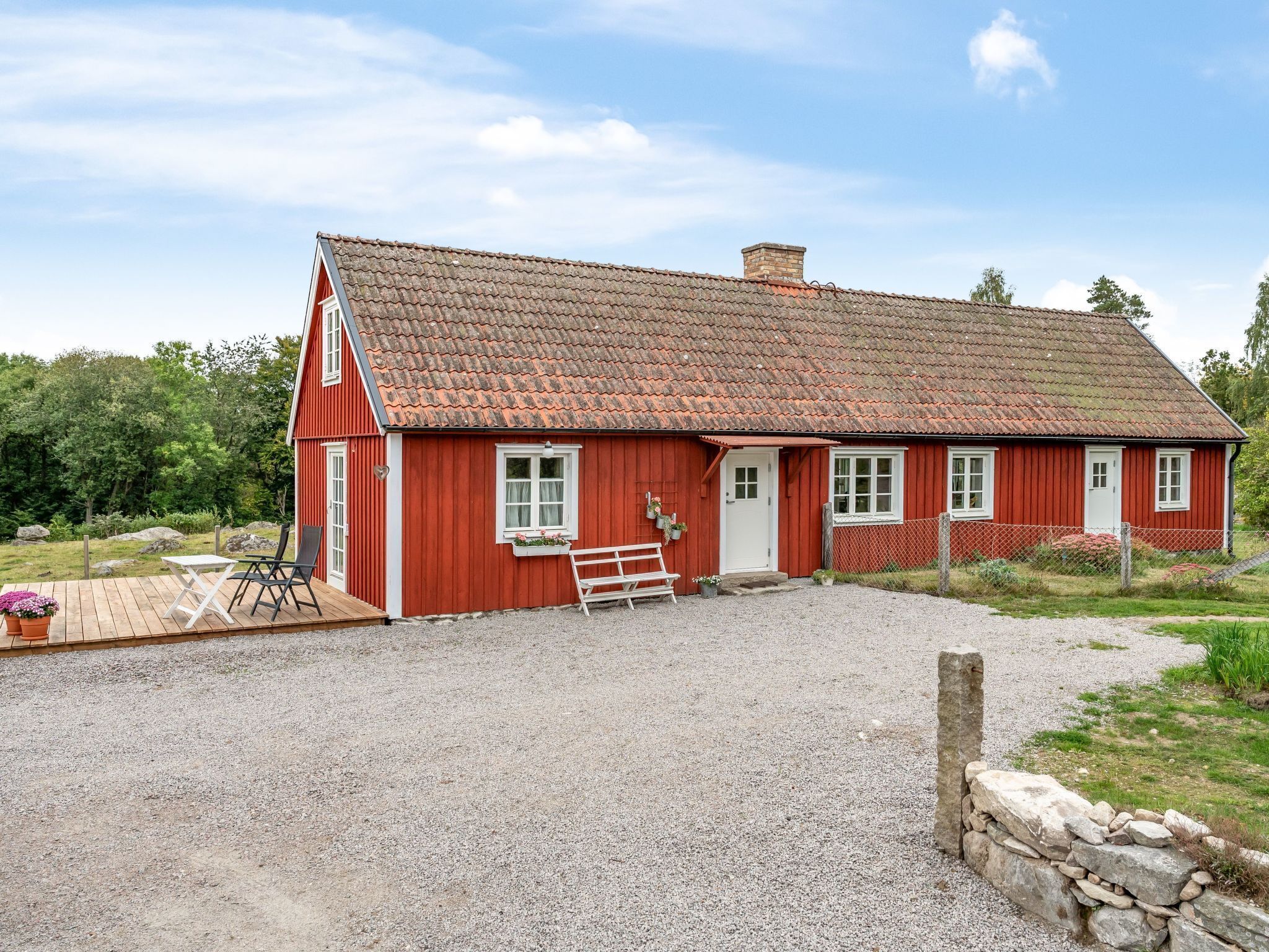 Una casa di legno rossa con vialetto sterrato e una panchina di legno.