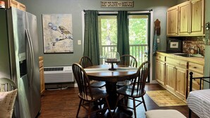 A cozy kitchen with wooden cabinets, a dining table with chairs, a refrigerator, and a window with curtains. - JayBird's Nest at Rumbling Bald in Lake Lure w/ pools, sauna, lake, spa, golf  (Lake Lure)