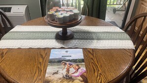 A wooden dining table with a placemat, a glass dome with cupcakes, and a planning guide on it. - JayBird's Nest at Rumbling Bald in Lake Lure w/ pools, sauna, lake, spa, golf  (Lake Lure)