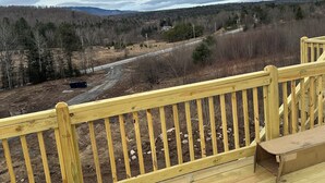 A wooden deck with a view of a forested area and a road in the distance. - ADK cottage with Mountain Views  (Saranac)