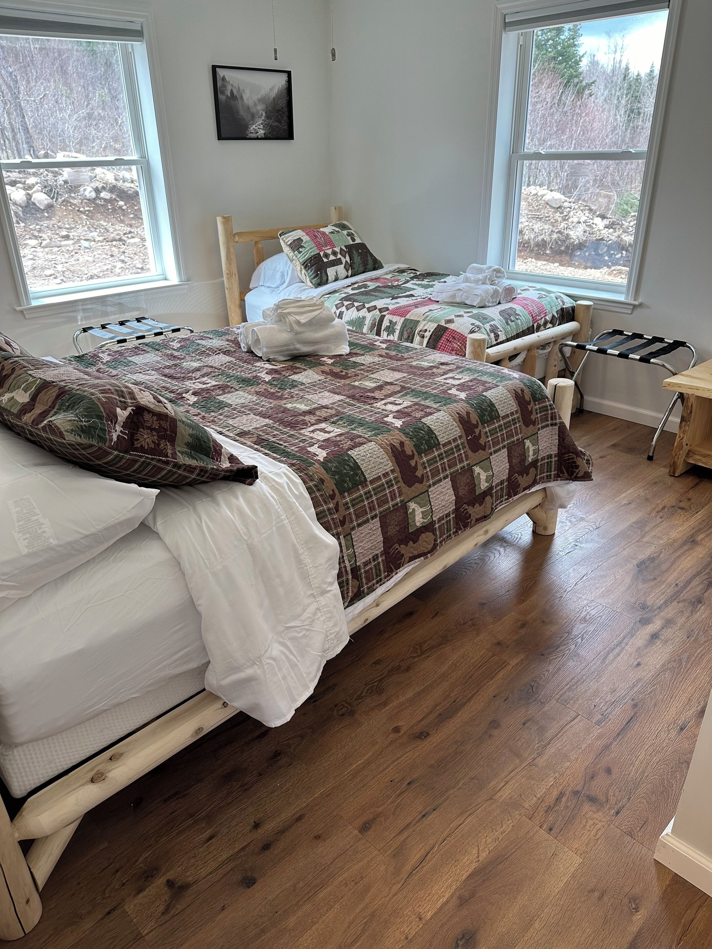 Een slaapkamer met twee houten bedden, een houten vloer en een raam met uitzicht op bomen.