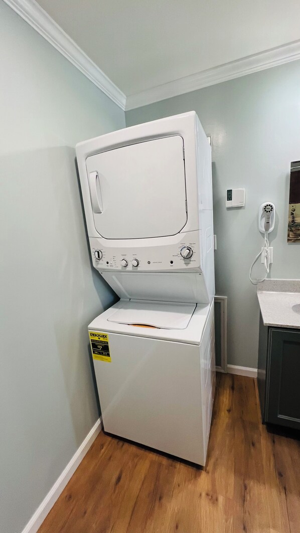 A compact washer and dryer unit in a laundry room with a wooden floor and light gray walls. - ADK cottage with Mountain Views (Saranac)