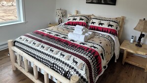 A bedroom with a bed, a nightstand, a lamp, and a window with a view of trees. - ADK cottage with Mountain Views  (Saranac)