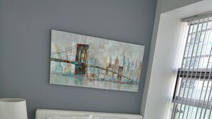 A neatly arranged bedroom with a large bed, a bedside table with a lamp, and a cityscape painting on the wall. -  Breathtaking view, as well as modern, clean & well-appointed apartment 
 

 (Toronto)