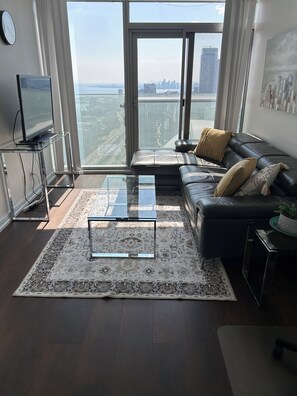 A modern living room with a leather sofa, a glass coffee table, and a view of the city skyline through large windows. -  Breathtaking view, as well as modern, clean & well-appointed apartment 
 

 (Toronto)