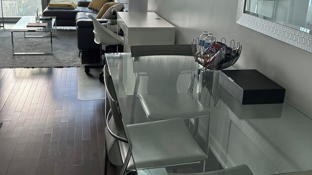 A modern living room with a glass dining table, leather sofa, and a large window offering a city view. -  Breathtaking view, as well as modern, clean & well-appointed apartment 
 

 (Toronto)