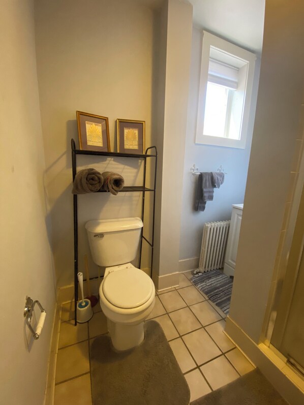 A bathroom with a toilet, a towel rack with towels, a radiator, and a window.