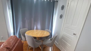 A room with a round wooden table, four grey chairs, a red sofa, a white door, and a window with curtains.