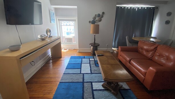 A living room with a TV, a brown leather sofa, a coffee table, and a patterned rug.