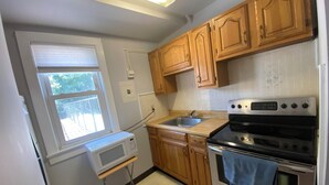 A compact kitchen with wooden cabinets, a built-in oven, a microwave, and a window.