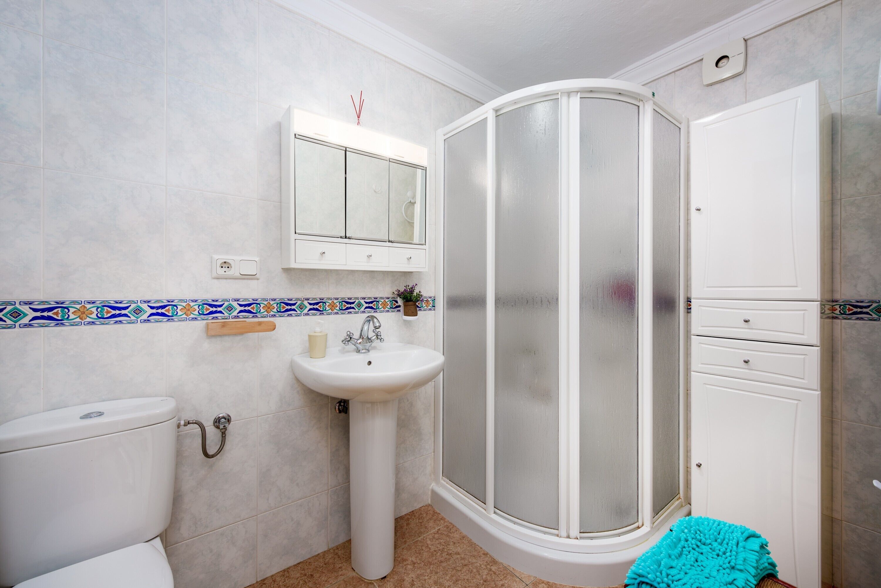 Ein Badezimmer mit Toilette, Waschbecken, Spiegel, Duschkabine und einem Schrank.
