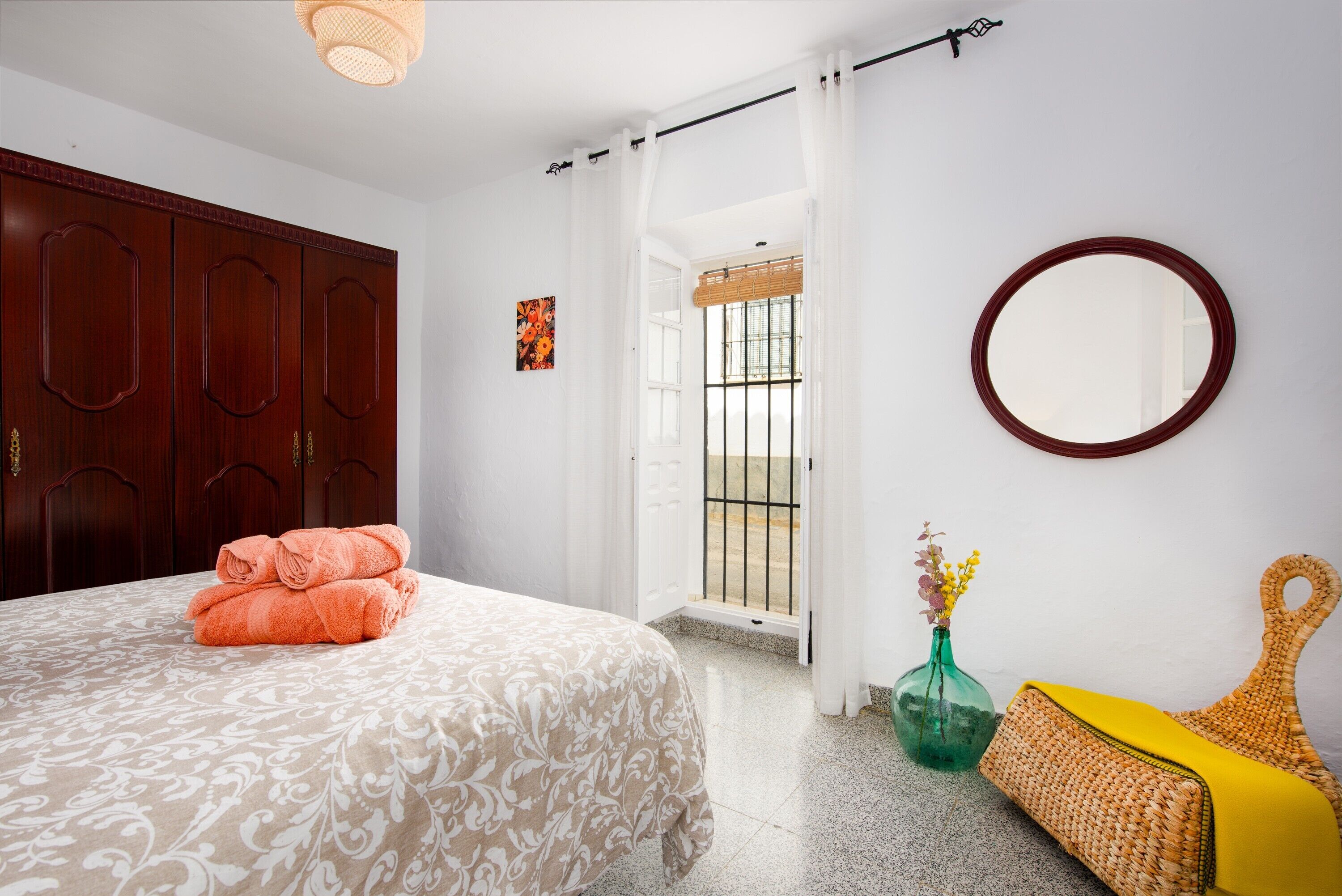 A bedroom with a bed, a wardrobe, a mirror, a window with a view, and a door leading to an outdoor area.