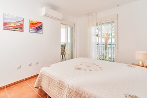 Een slaapkamer met een bed, twee schilderijen, een balkon en uitzicht op zee.