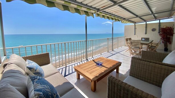 A covered outdoor seating area with a view of the ocean, a wooden table, wicker furniture, and a railing.