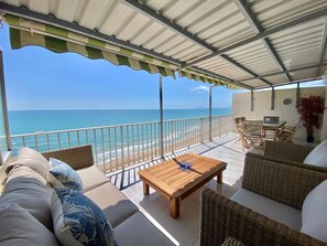 A covered outdoor seating area with a view of the ocean, a wooden table, wicker furniture, and a railing. - Flamingo Apartment with Sea Views, Private Terrace, and Wi-Fi (Tavernes de la Valldigna)