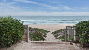 A beach entrance with a gate, sandy path, and ocean view.