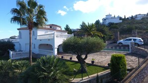 Une villa blanche à la façade en pierre, une allée bordée d’une clôture et une voiture garée.