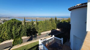 Un balcon offrant une vue sur un paysage côtier, avec des arbres et une étendue d’eau visible au loin.