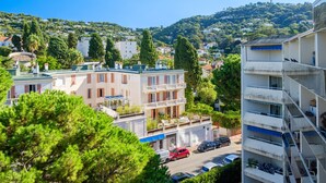 A residential area with multi-story buildings, a street with parked cars, and a hill with greenery in the background. - Apartment 'Sea and Sky 6 Personnes' with Mountain View, Private Terrace and Air Conditioning (Cannes)