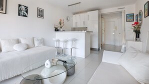 A modern, white-themed living area with a sofa, a glass coffee table, and a kitchen in the background. - Apartment 'Sea and Sky 6 Personnes' with Mountain View, Private Terrace and Air Conditioning (Cannes)