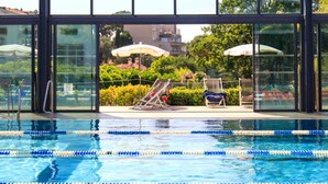 A swimming pool with clear lane dividers, surrounded by lounge chairs and umbrellas, with a view of greenery and buildings through large windows. - Apartment 'Sea and Sky 6 Personnes' with Mountain View, Private Terrace and Air Conditioning (Cannes)