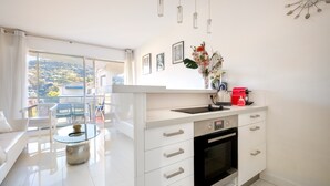 A modern kitchen with a built-in oven, a glass coffee table, and a view of a balcony with outdoor furniture. - Apartment 'Cannes Center Sea and Sky' with Sea View, Private Terrace and Air Conditioning (Cannes)