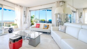 A modern living room with a glass coffee table, white sofas, and large windows offering a view of the city. - Apartment 'Cannes Center Sea and Sky' with Sea View, Private Terrace and Air Conditioning (Cannes)