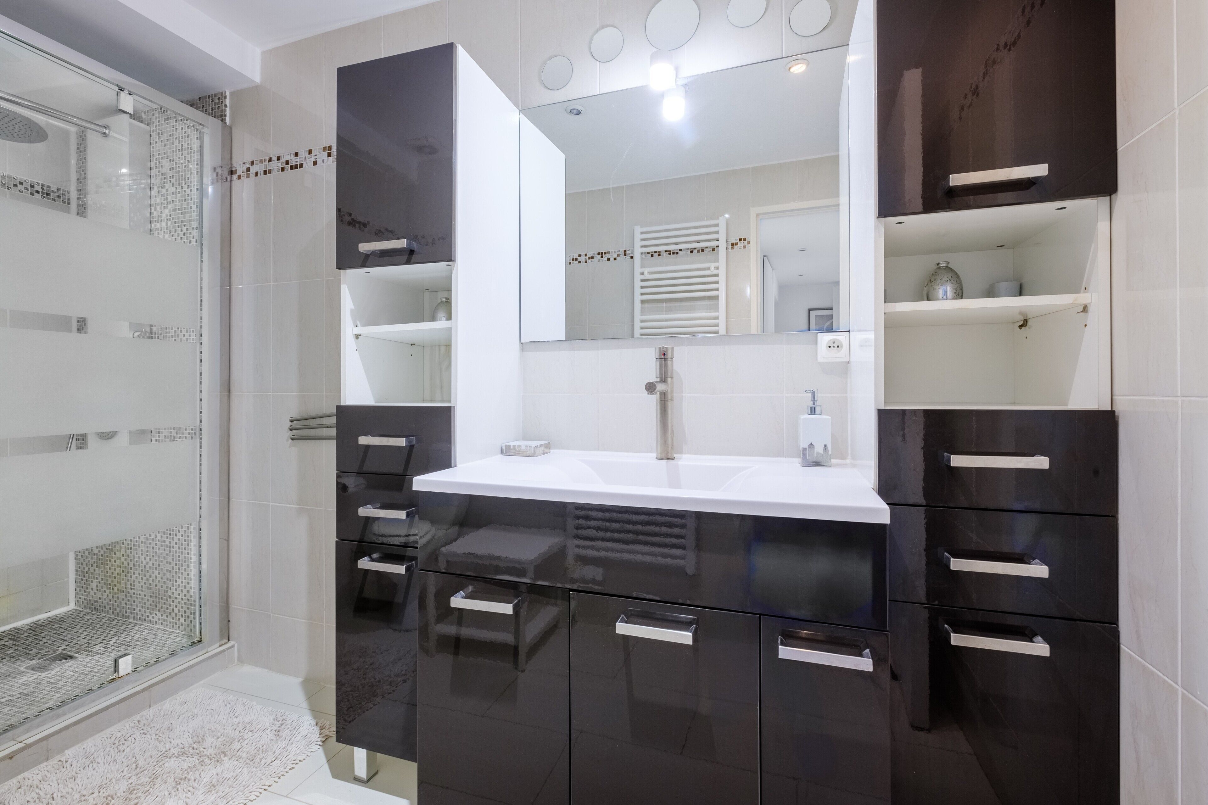 A modern bathroom with a glass shower enclosure, a white sink, and dark cabinetry.