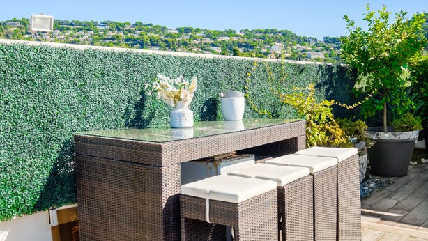 A wicker outdoor seating area with a glass-top table, a white vase with flowers, and a potted plant. - Apartment 'Cannes Center Sea and Sky' with Sea View, Private Terrace and Air Conditioning (Cannes)