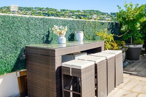 A wicker outdoor seating area with a glass-top table, a white vase with flowers, and a potted plant. - Apartment 'Cannes Center Sea and Sky' with Sea View, Private Terrace and Air Conditioning (Cannes)