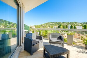 Uma varanda com móveis de vime, uma porta de vidro e vista para uma encosta verde.