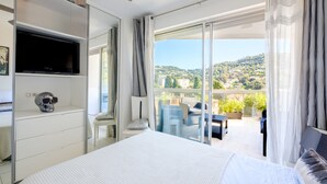 A bedroom with a bed, a TV, a skull decoration, a bedside table, and a view of an outdoor balcony with chairs and plants. - Apartment 'Sea and Sky 8 Personnes' with Sea View, Private Terrace and Air Conditioning (Cannes)