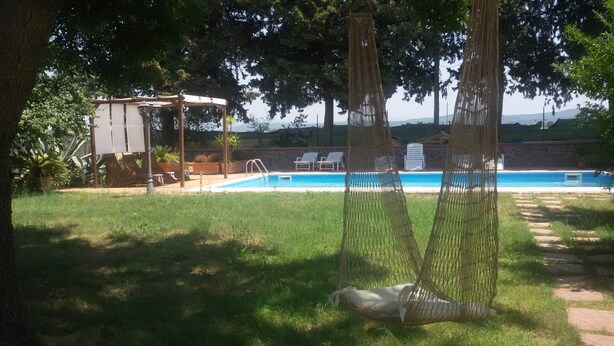 A backyard with a swimming pool, a hammock, and a pergola.