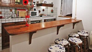 A kitchen with wooden cabinets, a central island with stools, a hanging light fixture, and a window with curtains.