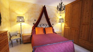 Une chambre à coucher avec un lit à baldaquin, deux lampes de chevet, un fauteuil, une armoire en bois et un lustre.