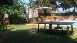 Un espace aménagé au bord de la piscine, comprenant une table de ping-pong, un jeu de fléchettes et une pergola décorée de guirlandes lumineuses.