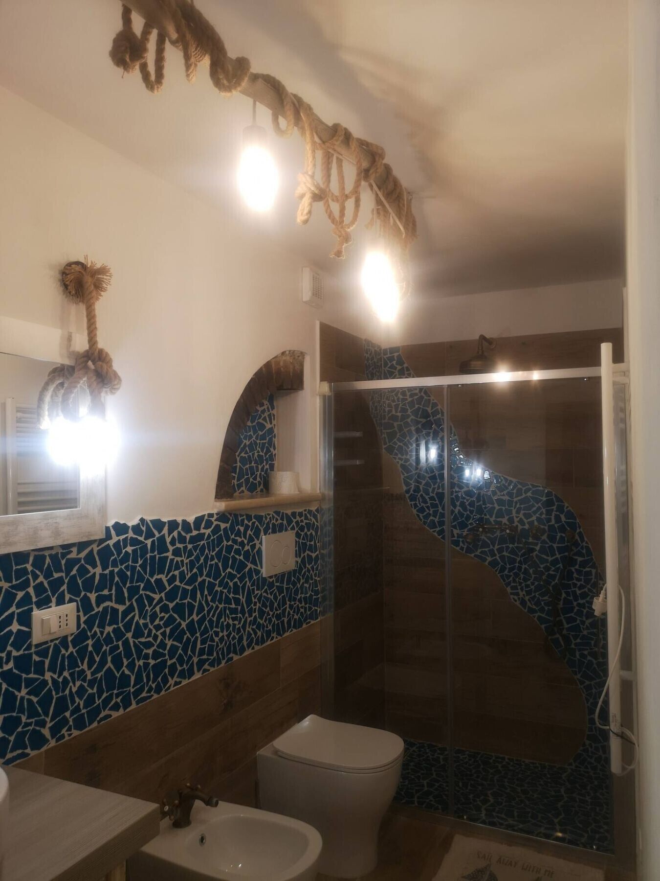 Un baño con pared de mosaicos, un inodoro, un lavamanos y una ducha con puerta de vidrio.
