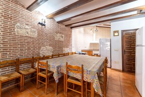 Un comedor con una mesa larga, sillas de madera, pared de ladrillo y techo de madera.